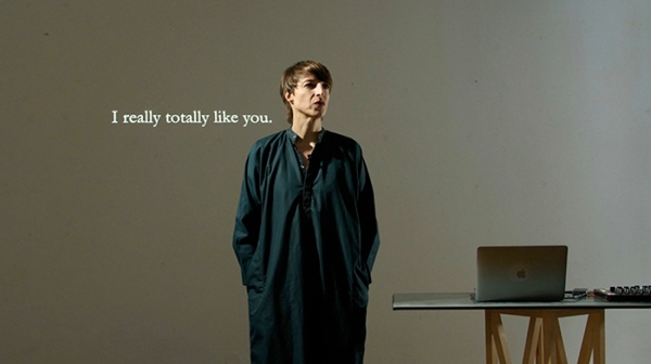 Intensity in Language (still), Frau vor einer Leinwand,
                                          am Tisch steht ein Laptop