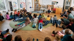 Kinder sitzen in einem Klassenzimmer am Boden vor einer Lehrerin