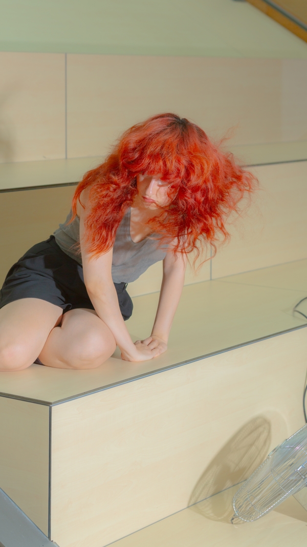 Eine Person mit langen roten Haaren kniet auf einer hölzernen Plattform.