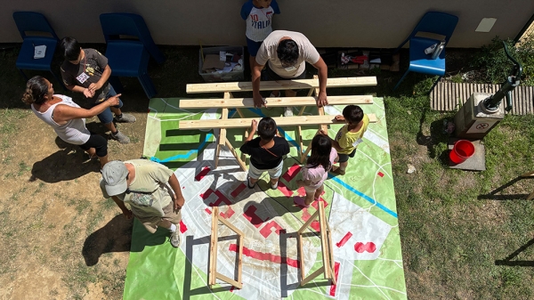 Kinder und Erwachsene arbeiten an einem Holzobjekt im Freien, , Summer School im Rahmen des Projekts Lunik CoLab