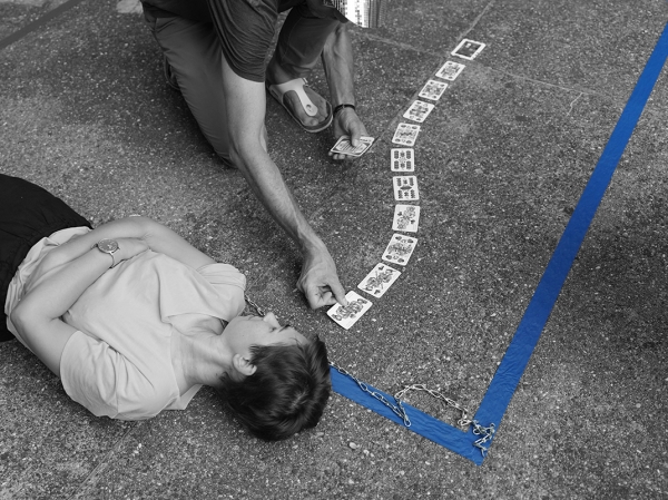 Eine Person liegt auf dem Boden.
                                          Neben ihr legt eine andere Person Spielkarten auf.