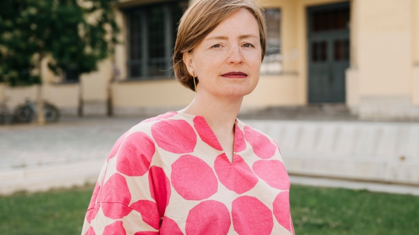 Porträt in Farbe von Ulrike Kuch vor grüner Wiese und einem Gebäude im Hintergrund