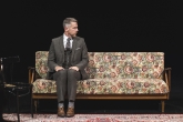 Der Performer Jim Libby auf einem Sofa auf einer dunklen Bühne