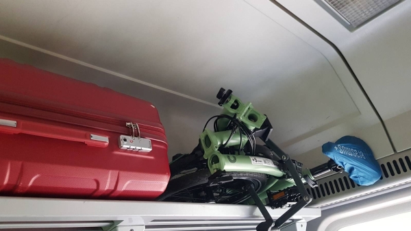 Klappfahrrad im Gepäckträger des Zuges leicht verstaut, Erasmus+ Sattelschutz sichtbar