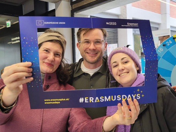 Drei Personen halten einen Erasmus+ Rahmen und lächeln